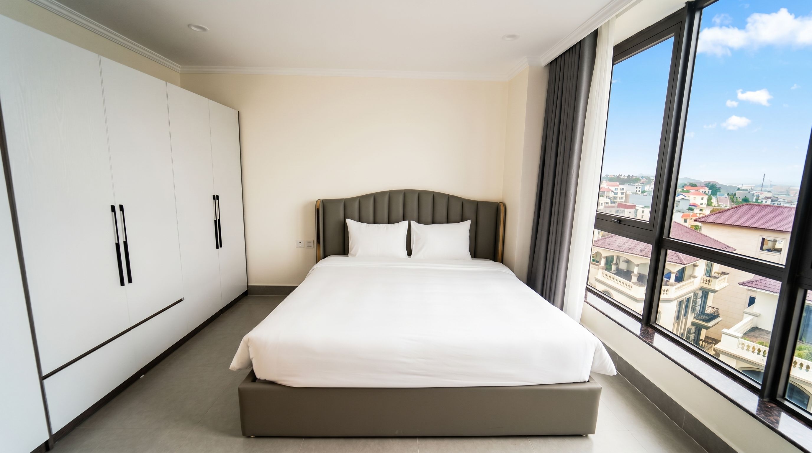 A hotel room with a large bed, a wardrobe, and a view of the city through a window.