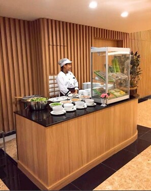 A reception desk with a chef, a glass display case with food items, and a potted plant. - Bangkok Eastern Hotel (Bang Bo)