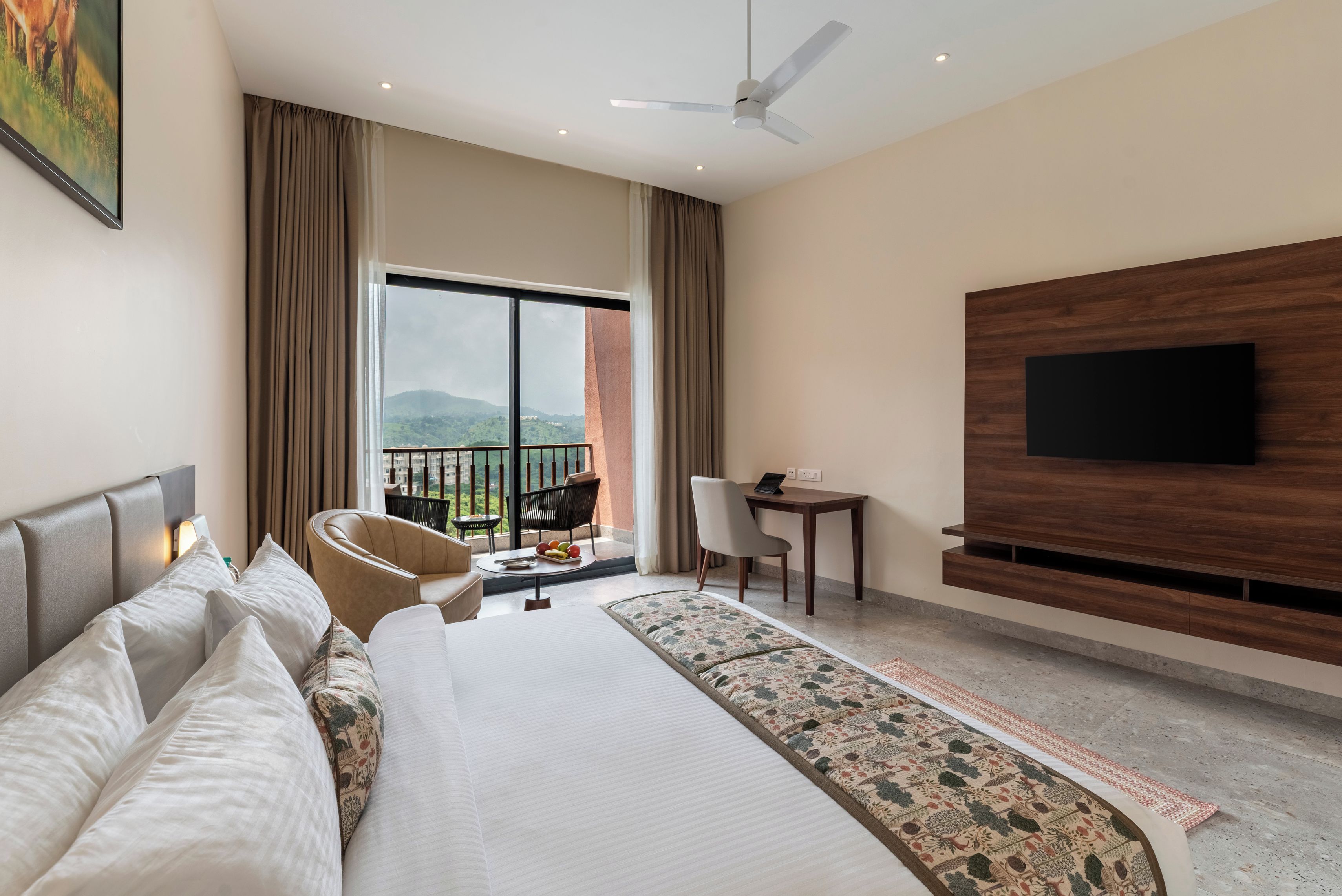 Habitación de hotel con una cama grande, un escritorio, una silla, un televisor y un balcón con vistas.