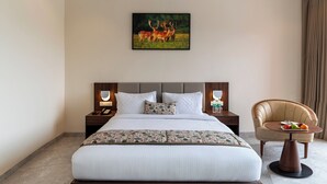 A hotel room with a large bed, a bedside table with a lamp, a chair with a fruit plate, and a picture of deer on the wall.