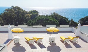 Terraza en la azotea con sillas blancas y cojines amarillos, con vistas al mar.