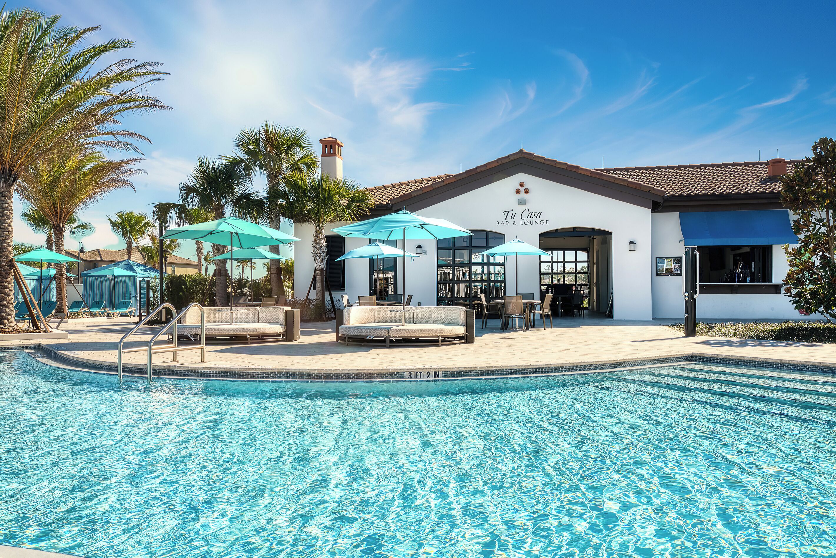 A pool area with lounge chairs and umbrellas, a bar & lounge building, and palm trees.