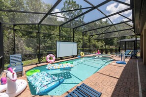 An outdoor swimming pool with a covered area, lounge chairs, and inflatable loungers. - Pool Movies|Game Room|Movie Theater|Private Lot (Kissimmee)