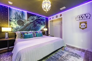 Ein Star Wars-Schlafzimmer mit einer großen Wandmalerei zum Thema Weltraum, einem Bett mit vielen Kissen und Star Wars-Sammlerstücken an den Wänden.
