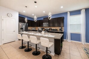 A modern kitchen with a central island, bar stools, dark cabinets, and a microwave. - Pool Movies|Game Room|Movie Theater|Private Lot (Kissimmee)