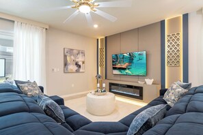 A modern living room with a ceiling fan, a flat-screen TV, a fireplace, and a large sofa set. - Breezy Palms|Spectacular NEW Villa|NEW WOW Resort (Clermont)