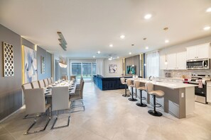 A modern kitchen with a central island, bar stools, and a dining area with a long table. - Breezy Palms|Spectacular NEW Villa|NEW WOW Resort (Clermont)