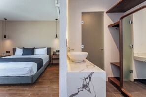 Une chambre moderne avec un lit, une table de chevet et une commode. On y trouve également une salle de bain équipée d’un lavabo, d’un miroir et d’une zone douche.