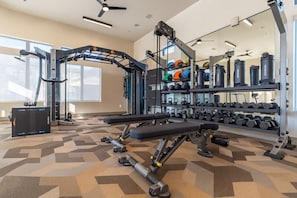 A gym with weightlifting equipment, kettlebells, and dumbbells. - Modern Apt I Prime Location & Workspace (Sherman)