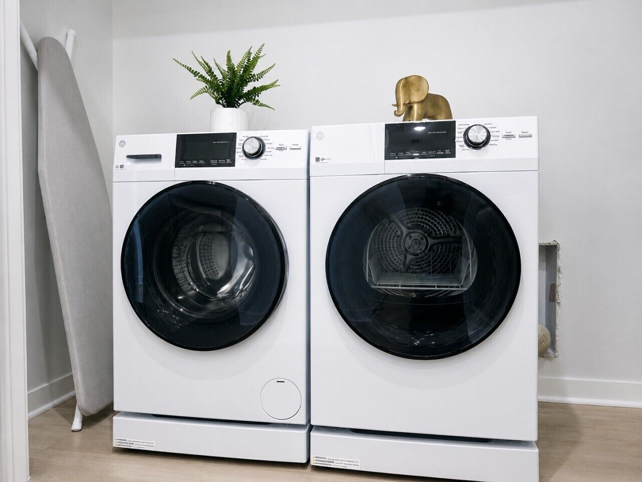 A pair of front-loading washing machines in a clean, modern laundry room with a potted plant and a decorative item on top.