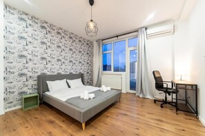 Une chambre à coucher avec un lit, un bureau, une chaise, une fenêtre et un mur décoré d’un motif.