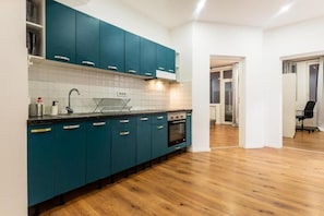 A modern kitchen with teal cabinets, a stainless steel sink, and a wood floor. - Spacious 4-bedroom apartment in lovely București with AC (București)