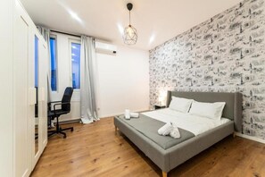 A modern bedroom with a grey bed, a desk with a chair, and a patterned wall. - Spacious 4-bedroom apartment in lovely București with AC (București)