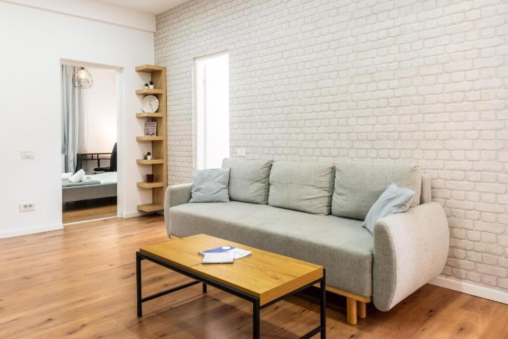 A modern living room with a grey sofa, a wooden coffee table, and a brick-patterned wall.