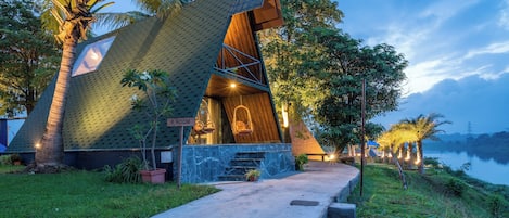 A modern house with a unique sloped roof, a concrete pathway leading to the entrance, and a serene lakeside setting.