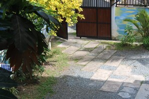 A paved pathway leading to a wooden gate, surrounded by greenery and a wall with a mural. - Catcus Reef Ahangama (Ahangama)
