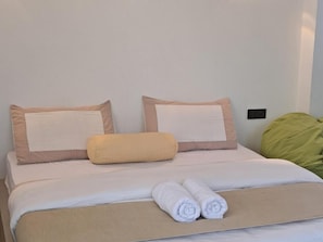 A neatly made bed with a beige bedspread, two pillows, and two rolled towels. - Catcus Reef Ahangama (Ahangama)