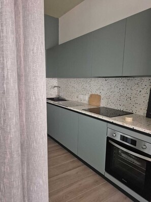 A kitchen with grey cabinets, a speckled backsplash, a sink, a cutting board, and an oven.
