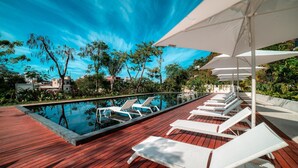 A poolside area with lounge chairs and umbrellas, surrounded by greenery and buildings. - Luxury 3BR Oasis | River & Ocean Views 3BD Condo for rent in El Caloso, Puerto v (Puerto Vallarta)