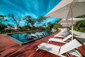 A poolside area with lounge chairs and umbrellas, surrounded by greenery and buildings. - Luxury 3BR Oasis | River & Ocean Views 3BD Condo for rent in El Caloso, Puerto v (Puerto Vallarta)