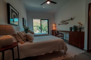 A bedroom with a bed, a desk, a chair, a lamp, and a view of the outdoors. - Luxury 3BR Oasis | River & Ocean Views 3BD Condo for rent in El Caloso, Puerto v (Puerto Vallarta)