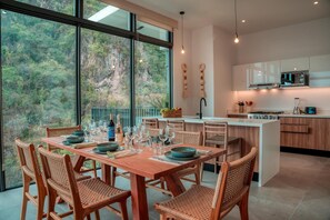 A modern kitchen with a dining area, large windows, and a view of the forest. - Luxury 3BR Oasis | River & Ocean Views 3BD Condo for rent in El Caloso, Puerto v (Puerto Vallarta)