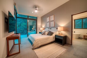 Ein modernes Schlafzimmer mit einem großen Bett, Nachttischen, einem Flachbildfernseher und Blick ins Freie.