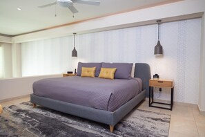 Un dormitorio moderno con una cama grande, dos mesitas de noche, un ventilador de techo y un papel tapiz estampado.