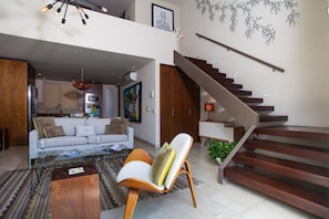 A modern living room with a sofa, coffee table, and a chair. There is a staircase with a wooden finish. - Designer Penthouse at V177 | Walk to Beach 1BD Condo for rent in Old Town, Puert (Puerto Vallarta)