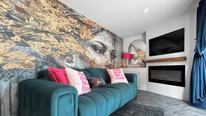 A teal sofa with multiple pillows, a large abstract painting on the wall, a fireplace, and a mounted TV. - 1 bedroom accommodation in Stranraer (Stranraer)