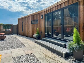 A modern wooden building with large glass windows, a gravel patio, and a metal fire pit. - 1 bedroom accommodation in Stranraer (Stranraer)