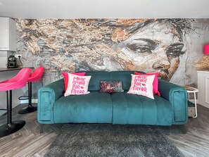 Ein türkisfarbenes Sofa mit zwei Kissen, einem gemusterten Zierkissen und einer Wand mit einem großen abstrakten Gemälde.