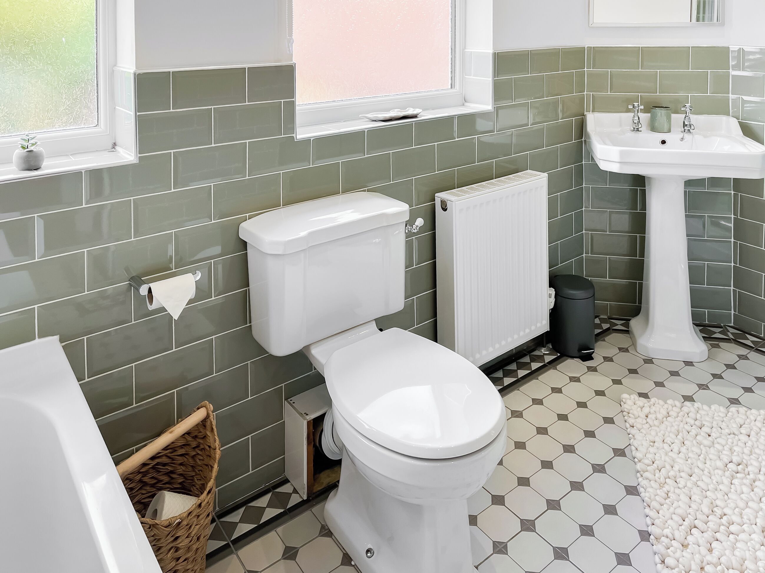 A bathroom with a toilet, a radiator, a sink, and a window.