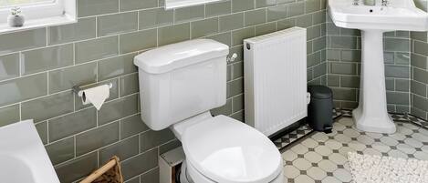 A bathroom with a toilet, a radiator, a sink, and a window.