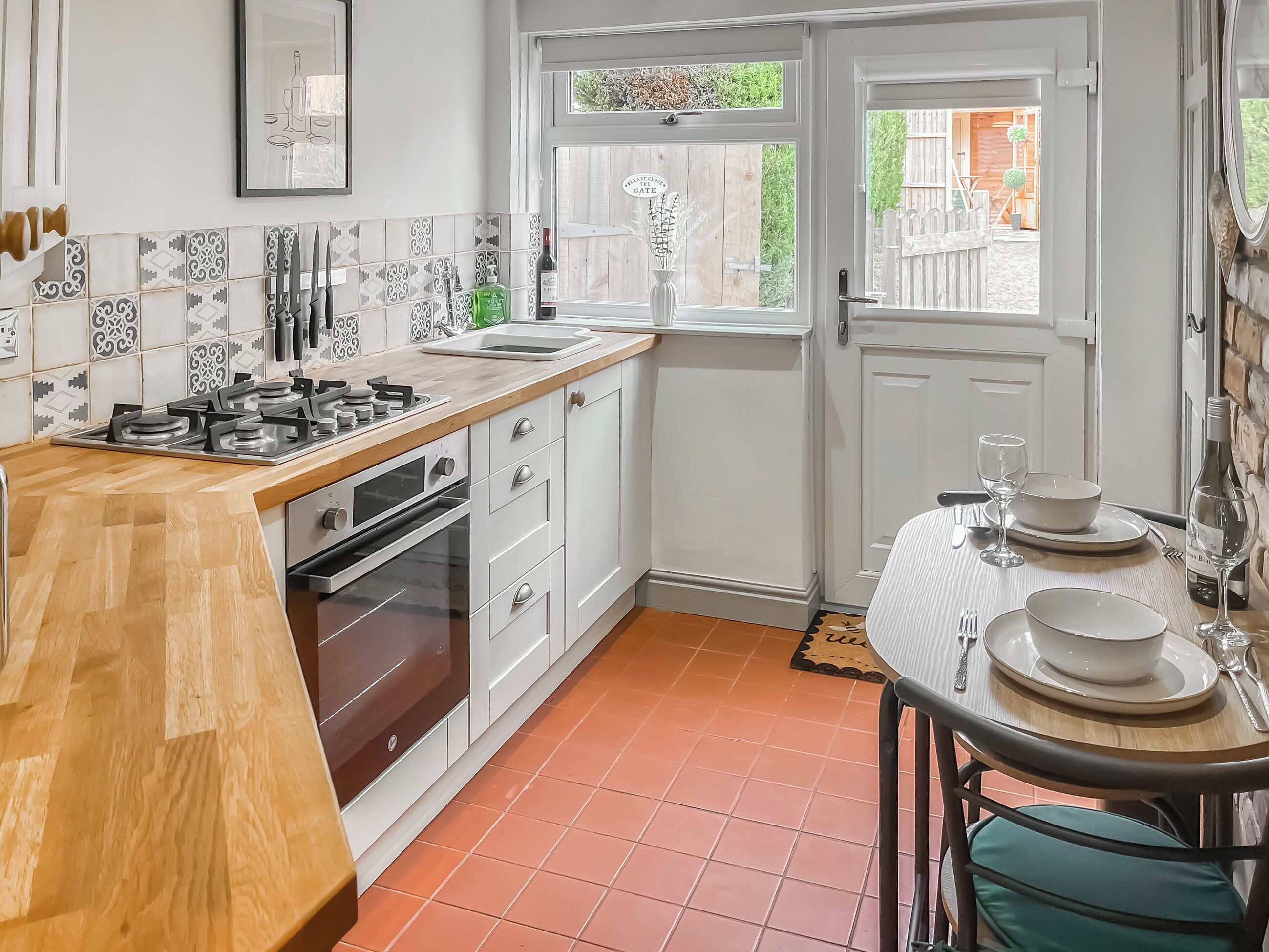 A kitchen with a wooden countertop, white cabinets, a dining area with a table set for two, and a window with a view of the outside.