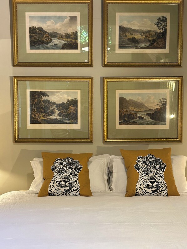 A bedroom with a bed, two pillows with a leopard print design, and four framed landscape paintings on the wall.