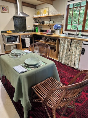 A dining area with a table set for two, a wicker chair, and a kitchen in the background.