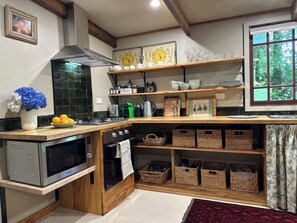 A kitchen with a built-in oven, a microwave, and a gas stove. There are shelves with dishes and a window with a view of greenery.