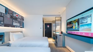 A hotel room with two beds, a TV mounted on the wall, and a desk with a computer.