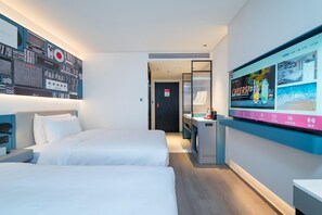 Une chambre d’hôtel avec deux lits, un téléviseur fixé au mur et un bureau avec un ordinateur.
