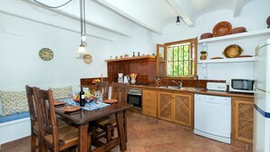 A kitchen with a dining table, chairs, a stove, a microwave, and a dishwasher. - Villa in Pollensa With Mountain Views & Pool (Pollença)