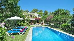 A swimming pool with lounge chairs and an umbrella, surrounded by greenery and a stone building. - Villa in Pollensa With Mountain Views & Pool (Pollença)