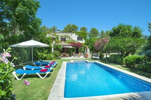 A swimming pool with lounge chairs and an umbrella, surrounded by greenery and a stone building. - Villa in Pollensa With Mountain Views & Pool (Pollença)