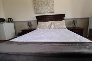 A hotel room with a bed, two bedside tables, a nightstand, a wall-mounted artwork, and a small white appliance.