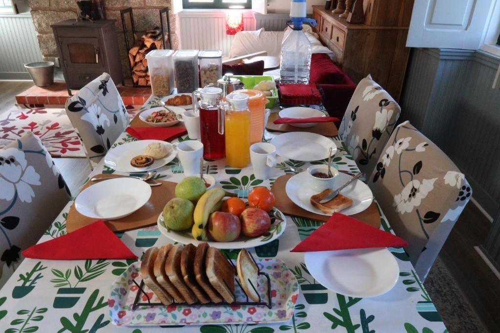 A dining table set with plates, cups, a pitcher, and a variety of fruits and bread.