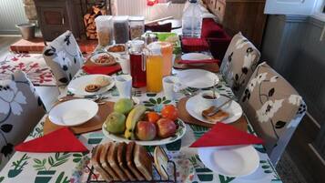 A dining table set with plates, cups, a pitcher, and a variety of fruits and bread.