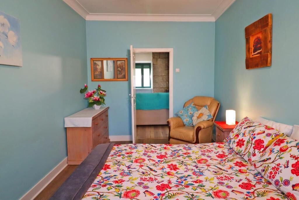 A bedroom with a bed, a chair, a dresser, and a door leading to another room.