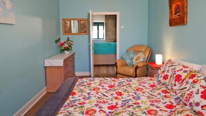 A bedroom with a bed, a chair, a dresser, and a door leading to another room.