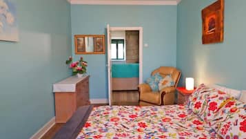 A bedroom with a bed, a chair, a dresser, and a door leading to another room.