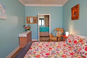 Ein Schlafzimmer mit einem Bett, einem Sessel, einer Kommode und einer Tür zu einem anderen Raum.